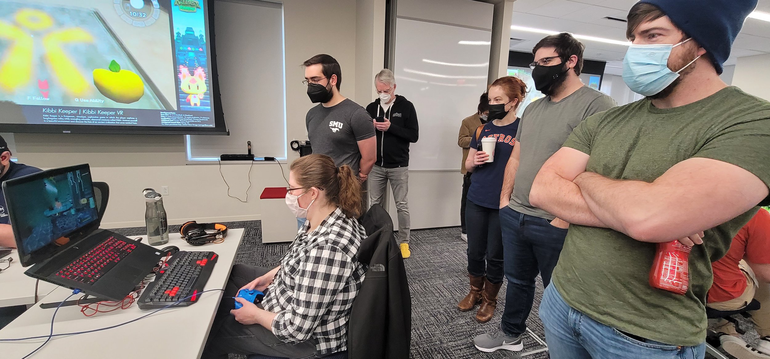Photo of someone playing AGRYOS: Recovering Eden. Behind them stand the developers, watching the gameplay.