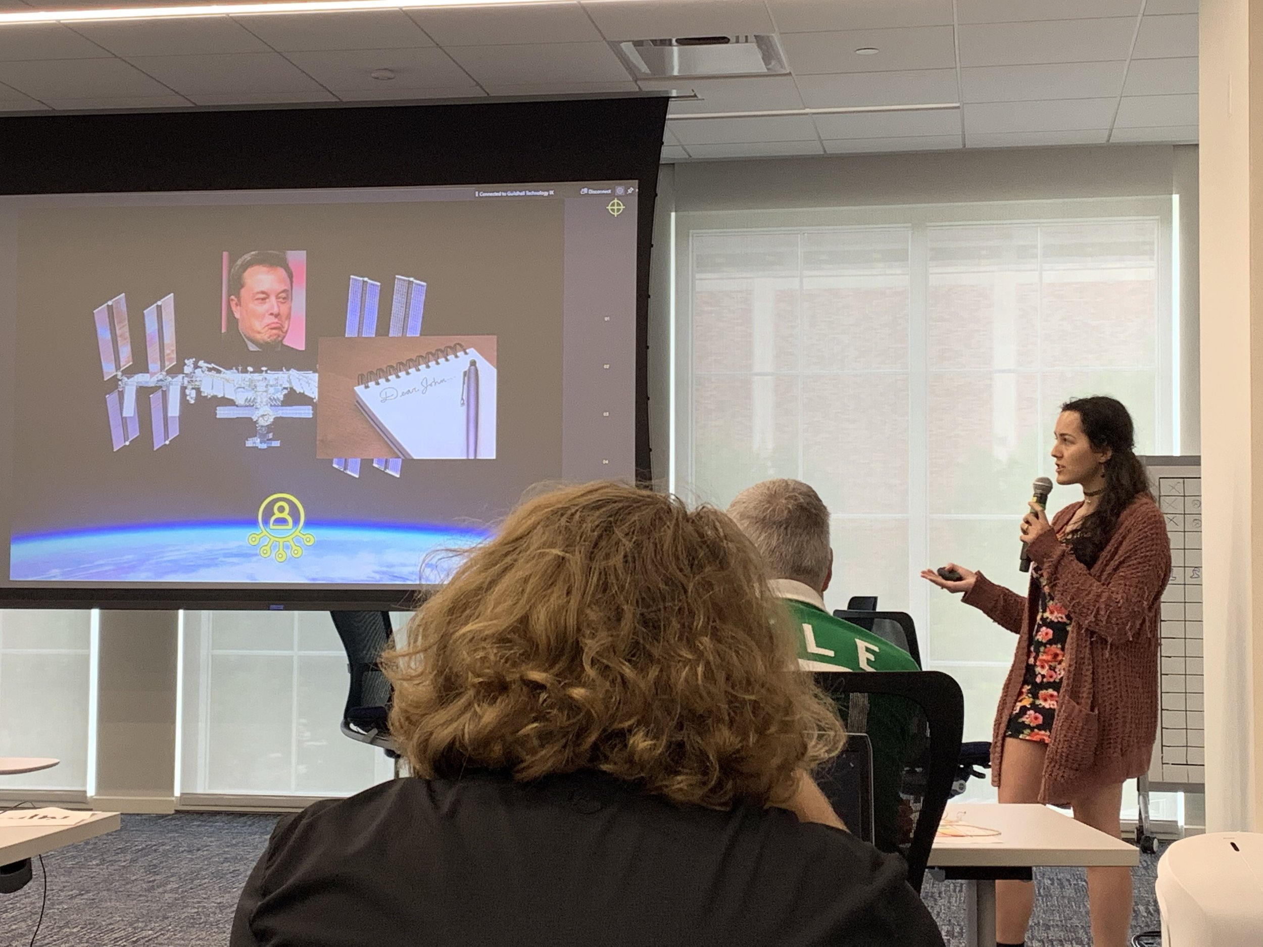 A photo of Nooka holding a microphone and giving a presentation.