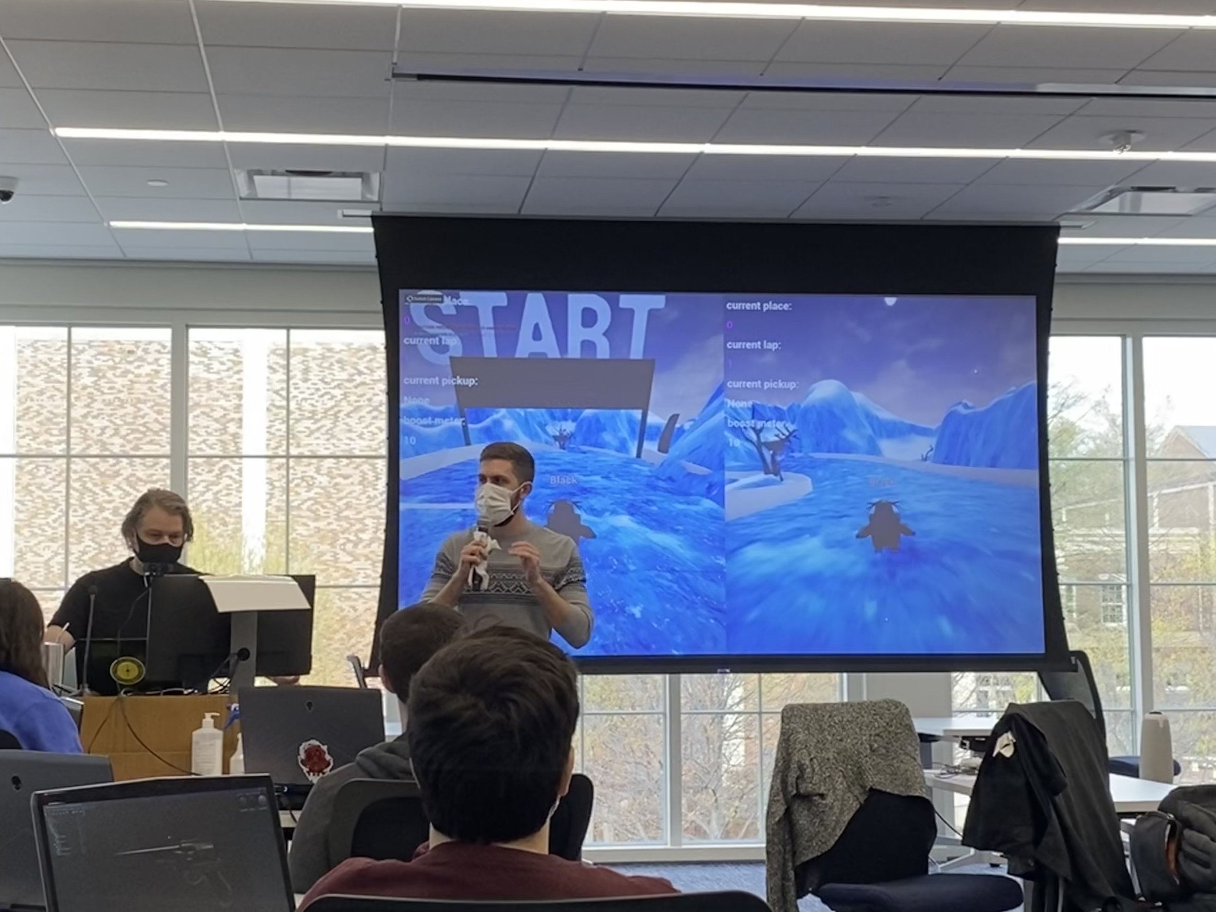 Dakota Loupe stands before the team, presenting Snowpainters' progress so far. Behind him, the presentation shows two penguins racing across the ice.